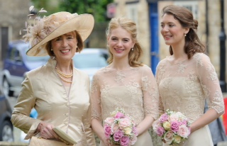 Bridesmaids in cream and gold dresses with matching fascinators, holding bouquets at a wedding