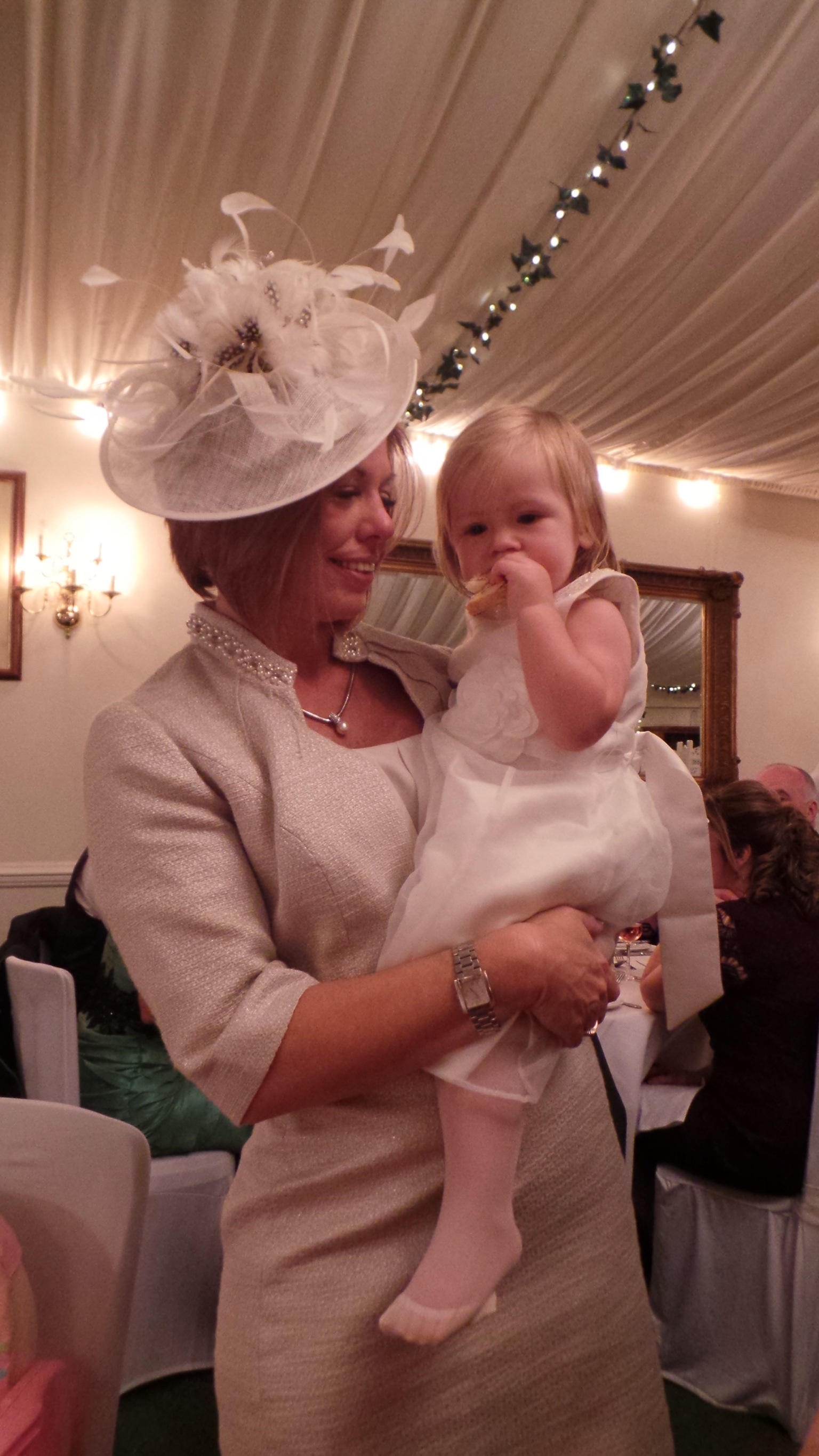 Wedding guest in a cream and champagne fascinator, holding a baby at the reception
