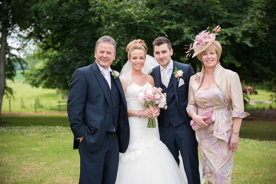 Wedding party group photograph, with the mother of the bride wearing a blush feathered fascinator