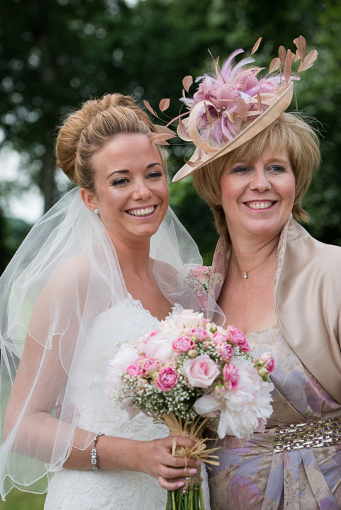 Bride and her mother, who is wearing a blush and gold feathered fascinator, holding her wedding bouquet