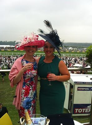 Two racegoers at Ascot wearing pink and navy fascinators, beside the Totepool enclosure