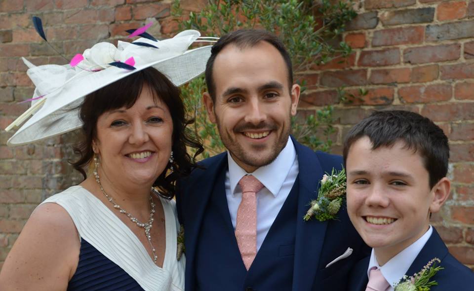 Mother of the groom wearing a cream and navy feathered fascinator, with the groom and best man