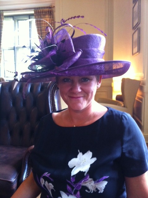 Client wearing a vivid purple wide-brimmed hat with feather trim from the hire wardrobe