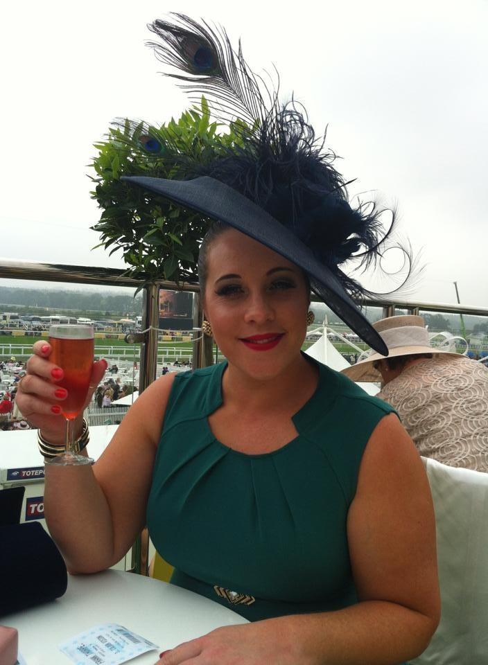 Race day guest wearing a striking navy fascinator trimmed with peacock feathers