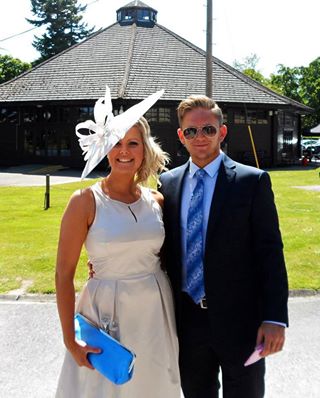 Wedding guest in a white dress with a delicate white fascinator, smiling beside her partner at a country house wedding venue