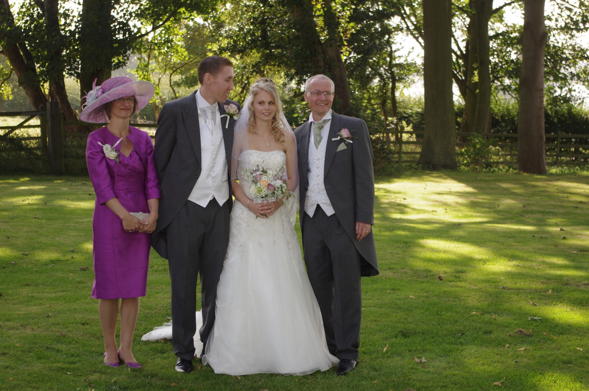 Mother of the bride wearing a pink wide-brimmed hat with feather trim, with the bride, groom and father of the bride