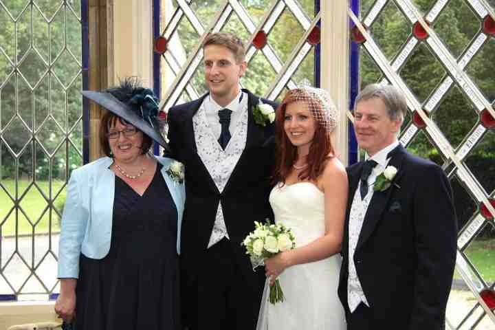 Mother of the bride wearing a navy hat with feather trim, with the bride, groom and father of the bride